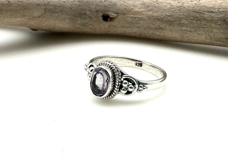 May include: A silver ring with a purple gemstone set in a decorative bezel. The ring has a twisted band and is marked "925" on the inside.