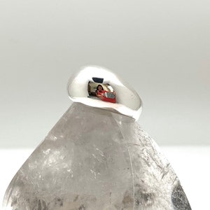 May include: A smooth, silver ring with a rounded, dome-shaped top. The ring is sitting on a white, textured surface.