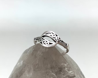 May include: A silver ring with an openwork design featuring two leaf-like shapes with swirling details. The ring is set against a light background, showcasing its intricate patterns and polished finish.