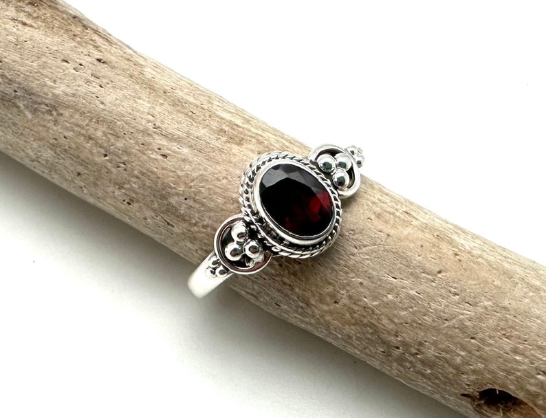 May include: A silver ring with a red gemstone set in a decorative bezel. The ring has a beaded design on the band.