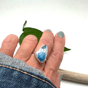 May include: A silver ring with a blue and white gemstone set in a triangular shape.
