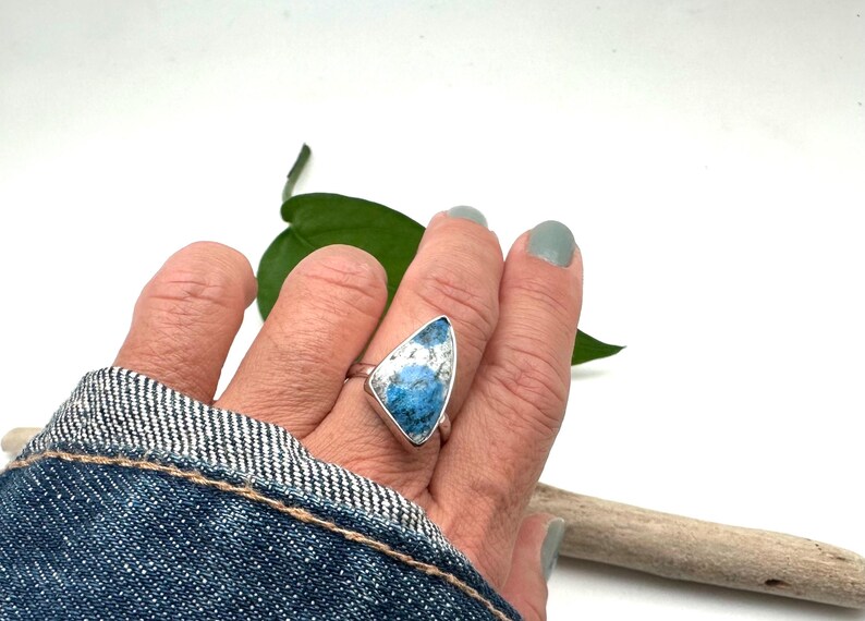 May include: A silver ring with a blue and white gemstone set in a triangular shape.