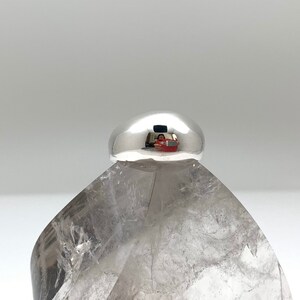 May include: A silver ring with a smooth, rounded top. The ring is sitting on a clear crystal.