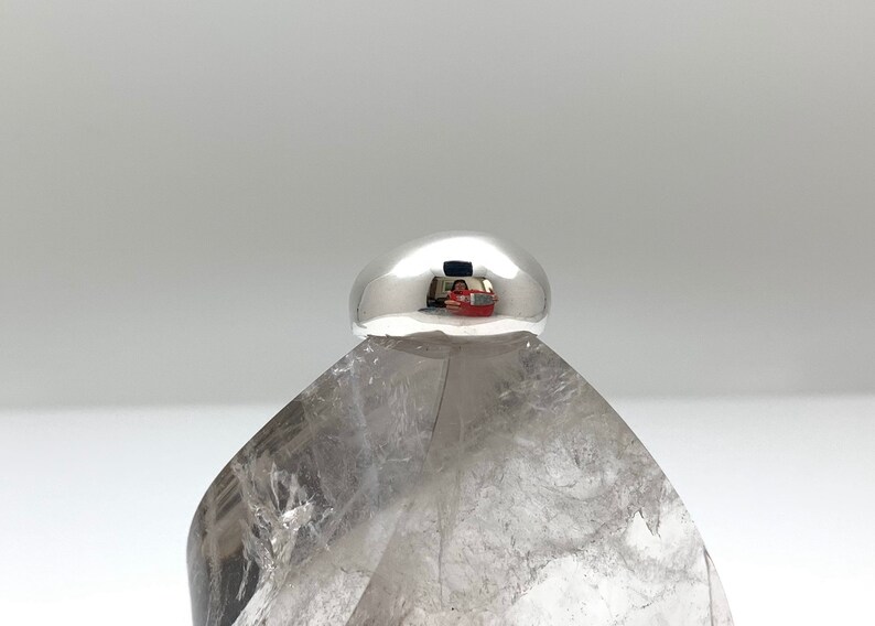 May include: A silver ring with a smooth, rounded top. The ring is sitting on a clear crystal.