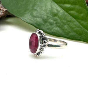 May include: A silver ring featuring a deep red oval gemstone set in an ornate filigree design.
