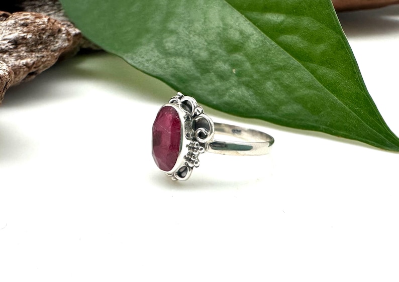 May include: A silver ring featuring a deep red oval gemstone set in an ornate filigree design.