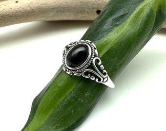 Op de afbeelding: Een zilveren ring met een ovale zwarte edelsteen gezet in een decoratief filigraanontwerp.