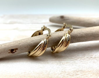 May include: A pair of gold hoop earrings with a textured, wavy design. The earrings are made of metal and have a hinged closure.