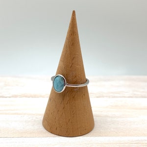 May include: A silver ring featuring a light blue oval gemstone. The ring is displayed on a wooden ring stand.