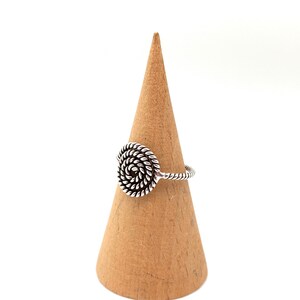 May include: A silver ring with a spiral design. The ring is on a wooden ring holder.