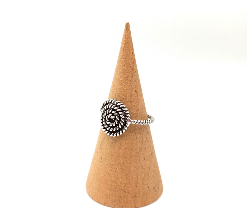 May include: A silver ring with a spiral design. The ring is on a wooden ring holder.