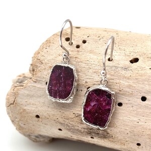 May include: A pair of silver earrings with a deep red, rectangular, raw ruby stone on each earring.