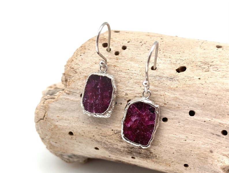 May include: A pair of silver earrings with a deep red, rectangular, raw ruby stone on each earring.