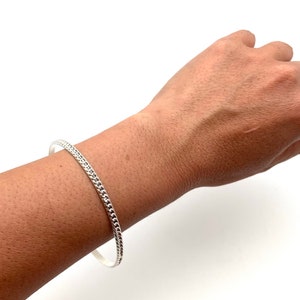 May include: A silver bangle bracelet with a textured design.