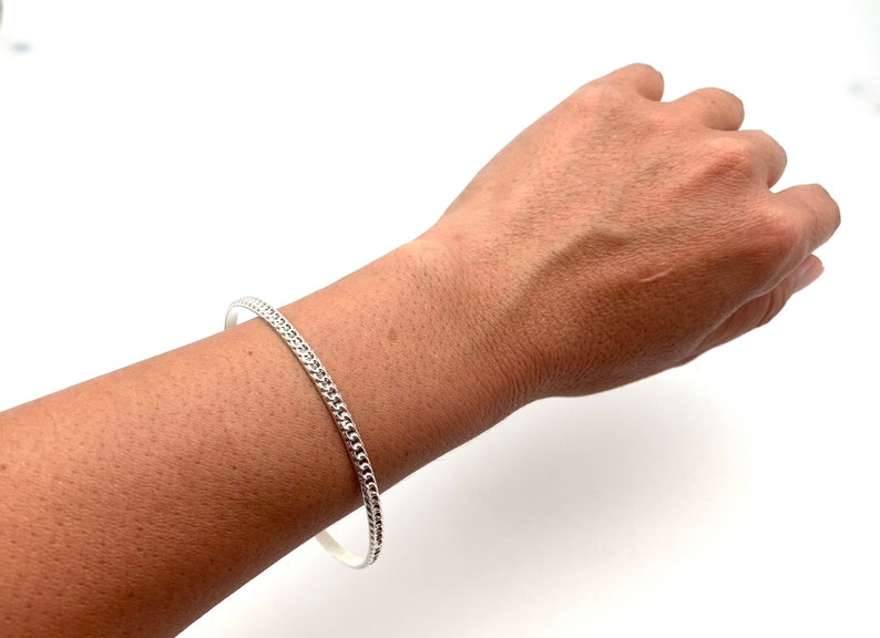 May include: A silver bangle bracelet with a textured design.