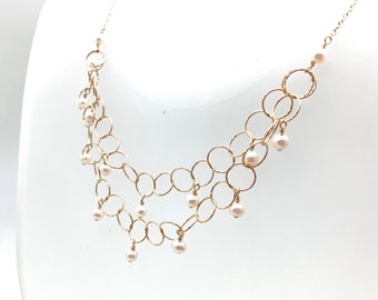May include: A gold necklace with a delicate chain design featuring multiple interconnected circles. The necklace is adorned with small white pearls hanging from the chain.
