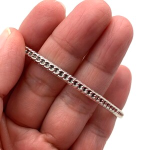 May include: A silver chain bracelet with a delicate, intricate design. The bracelet is shown on a hand, highlighting its size and fit.