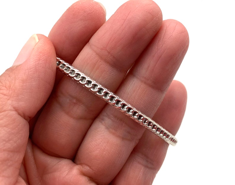 May include: A silver chain bracelet with a delicate, intricate design. The bracelet is shown on a hand, highlighting its size and fit.