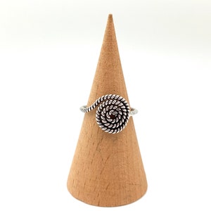 May include: Silver ring with a spiral design. The ring is displayed on a wooden ring holder.