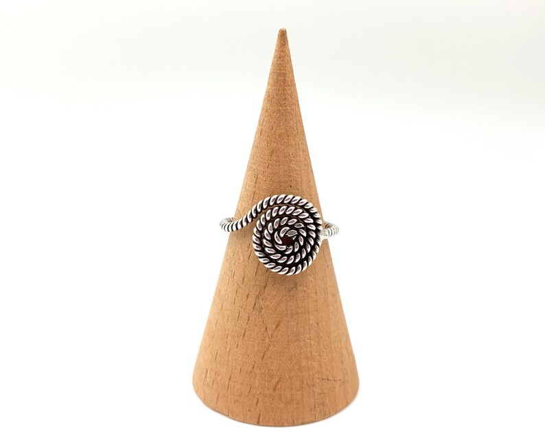 May include: Silver ring with a spiral design. The ring is displayed on a wooden ring holder.