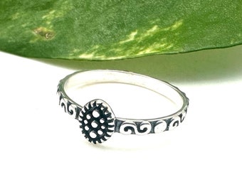 May include: A silver ring with a decorative design featuring a circular pattern in the centre and a swirl pattern around the band.