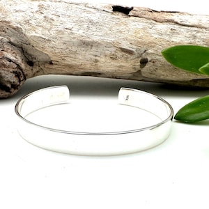 May include: A simple silver bangle bracelet with a smooth, polished finish. The bracelet is open ended and has a slight curve to it.