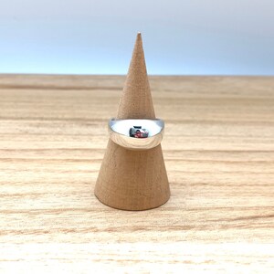 May include: A silver ring with a rounded, domed top. The ring is displayed on a wooden ring holder.