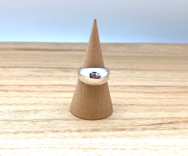 May include: A silver ring with a rounded, domed top. The ring is displayed on a wooden ring holder.