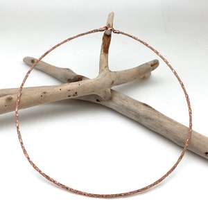 May include: A rose gold necklace with a delicate, braided chain design. The necklace is displayed on a piece of driftwood.
