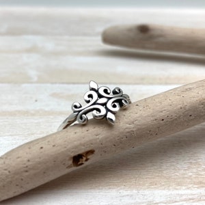Può includere: Un anello d'argento con un design delicato e ornato con motivi a spirale e foglie.