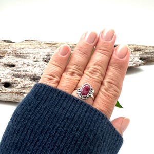 May include: A silver ring with a pink oval gemstone set in a floral design.