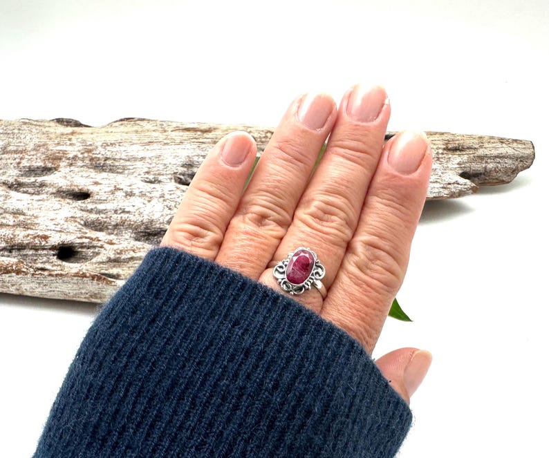 May include: A silver ring with a pink oval gemstone set in a floral design.