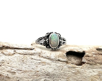 Könnte beinhalten: Ein silberner Ring mit einem ovalen Opal-Edelstein, der in einem floralen Design gefasst ist.