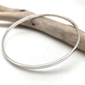 May include: A simple silver bangle bracelet. The bracelet is smooth and polished, with a slightly rounded edge.