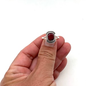 Op de afbeelding: Een zilveren ring met een rode edelsteen in een vierkante zetting. De ring heeft een parelrand rond de zetting.