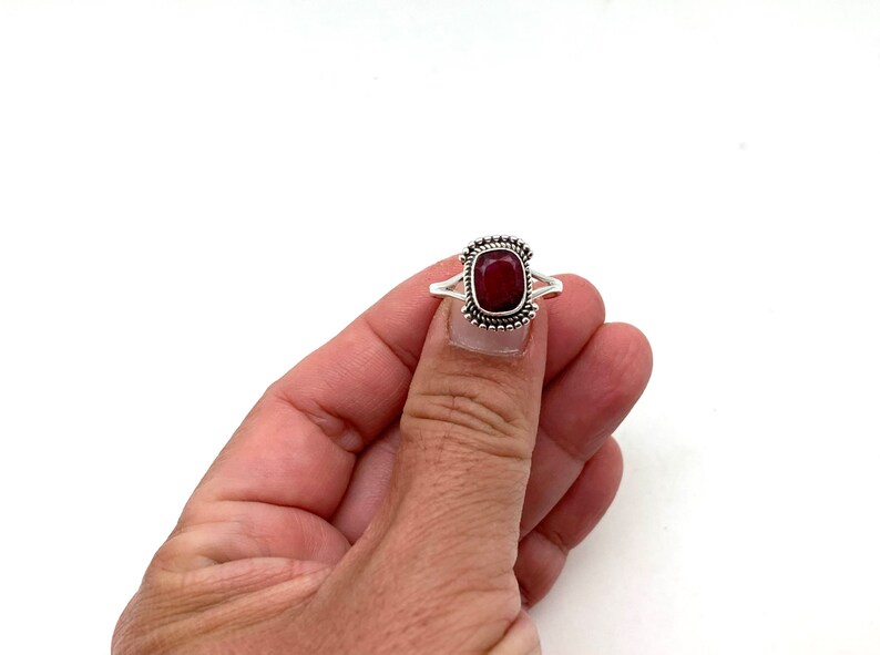 Op de afbeelding: Een zilveren ring met een rode edelsteen in een vierkante zetting. De ring heeft een parelrand rond de zetting.