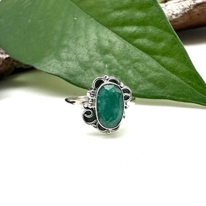 Puede incluir: Un anillo de plata con una piedra ovalada verde engastada en un diseño de filigrana decorativo.