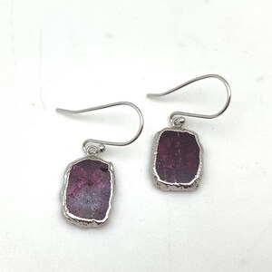 May include: A pair of silver earrings with a rectangular, dark purple gemstone set in each earring.