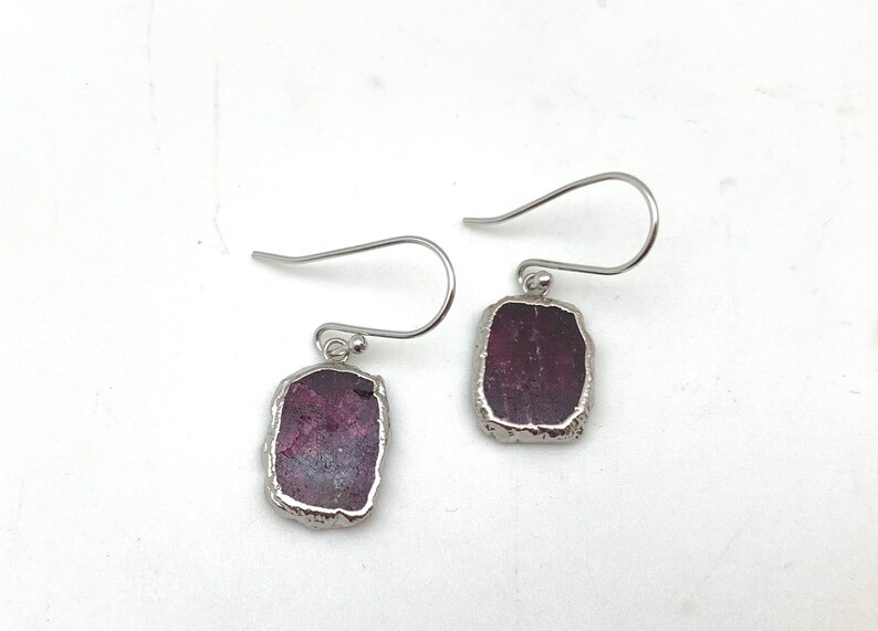 May include: A pair of silver earrings with a rectangular, dark purple gemstone set in each earring.