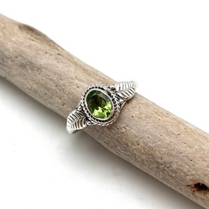 May include: A silver ring with a green gemstone set in a leaf design.