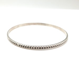 May include: A silver bangle bracelet with a textured design around the edge.