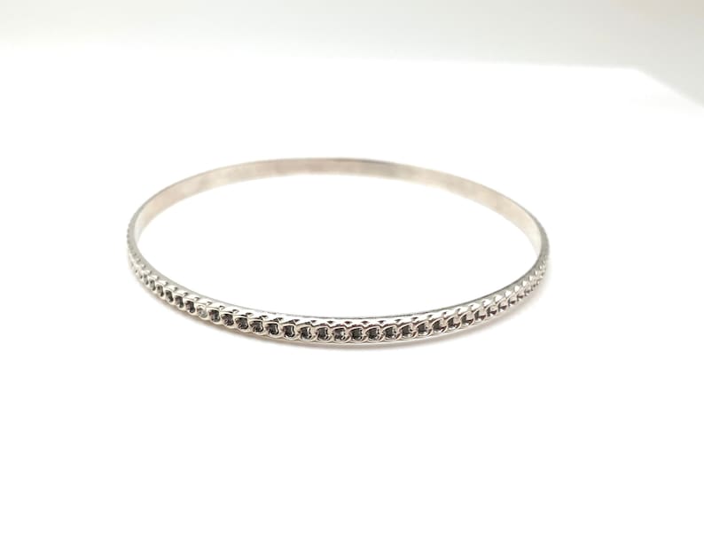 May include: A silver bangle bracelet with a textured design around the edge.