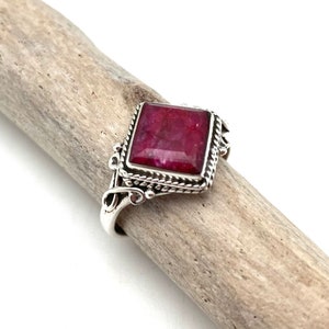 May include: A silver ring with a square-shaped red gemstone set in a decorative silver frame.