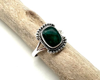 Puede incluir: Un anillo de plata con una piedra preciosa verde oscuro engastada en un engaste de cuentas. El anillo tiene una banda simple con una caña dividida.