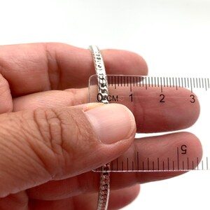 May include: A silver chain bracelet measured with a ruler, showing it is approximately 1 inch in diameter.