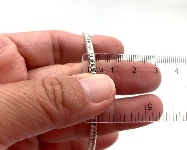 May include: A silver chain bracelet measured with a ruler, showing it is approximately 1 inch in diameter.