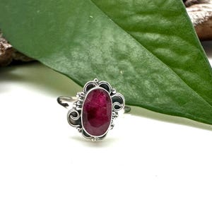 May include: A silver ring with an oval-shaped ruby gemstone set in a decorative filigree design.