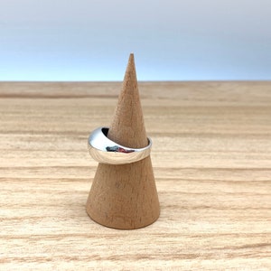 May include: A silver ring with a smooth, rounded design. The ring is displayed on a wooden ring holder.