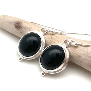 May include: A pair of silver earrings with black oval gemstones. The earrings have a simple design with a smooth, polished finish.