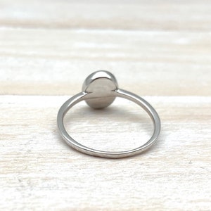 May include: A silver ring featuring a smooth, oval-shaped gemstone. The ring is simple and elegant.